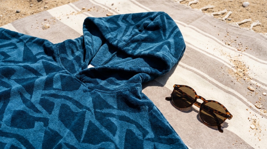 A hooded microfiber surf changing poncho laid out on a beach towel.
